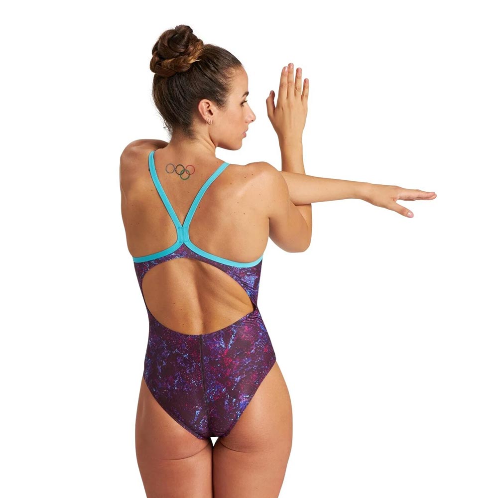 Back view of a woman wearing a purple pattern arena swimsuit with cyan straps.