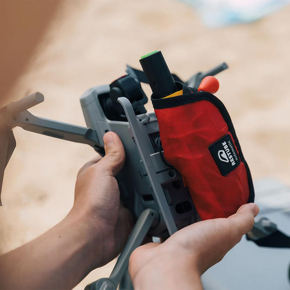 A person holding a drone, showing how the Restube Automatic water rescue device can be attached.