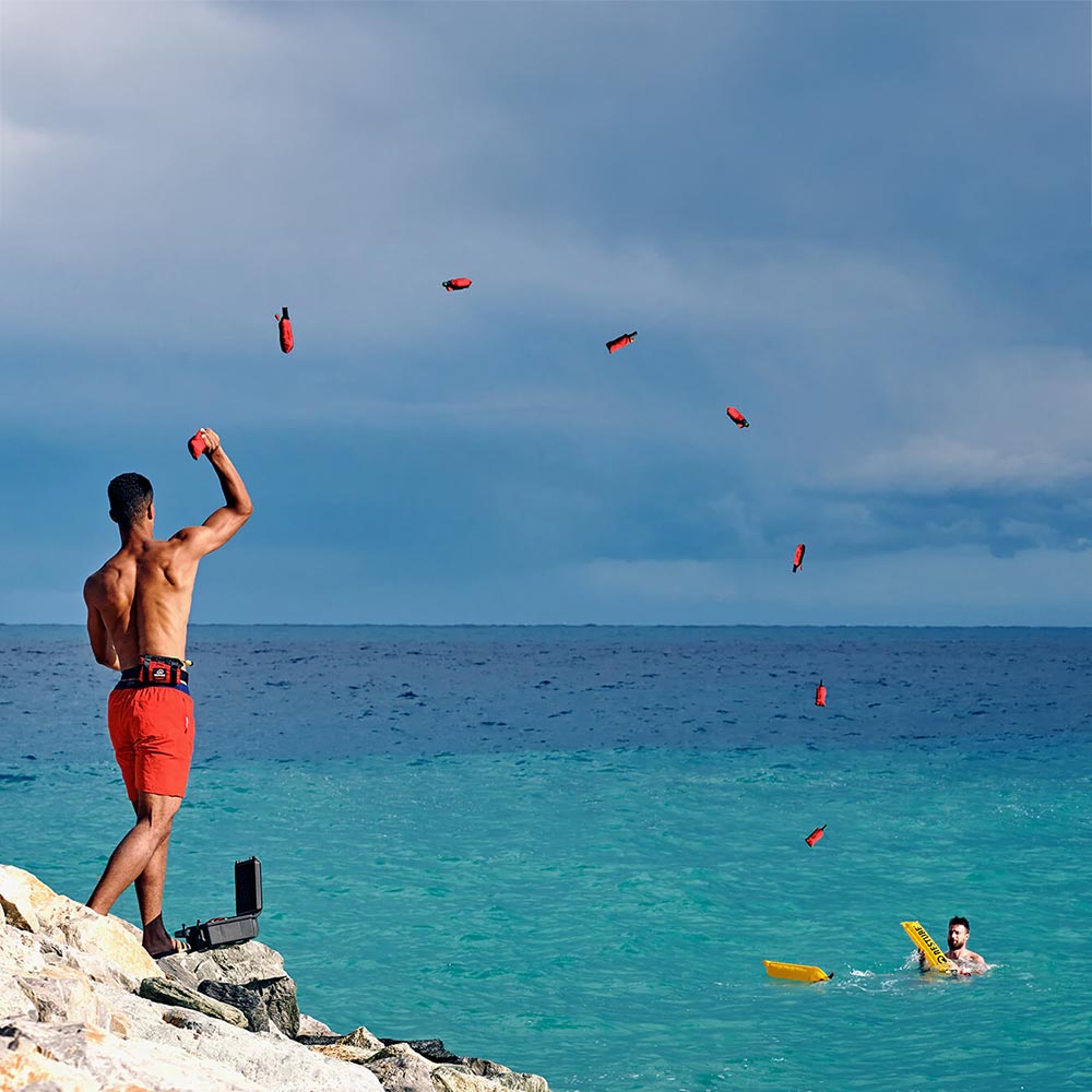 An image depicting a man throwing the Restube Automatic Waste Rescue Device at someone in the ocean needing assistance.