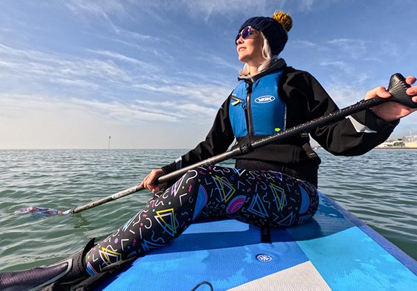 Woman in life vest paddleboarding in calm water