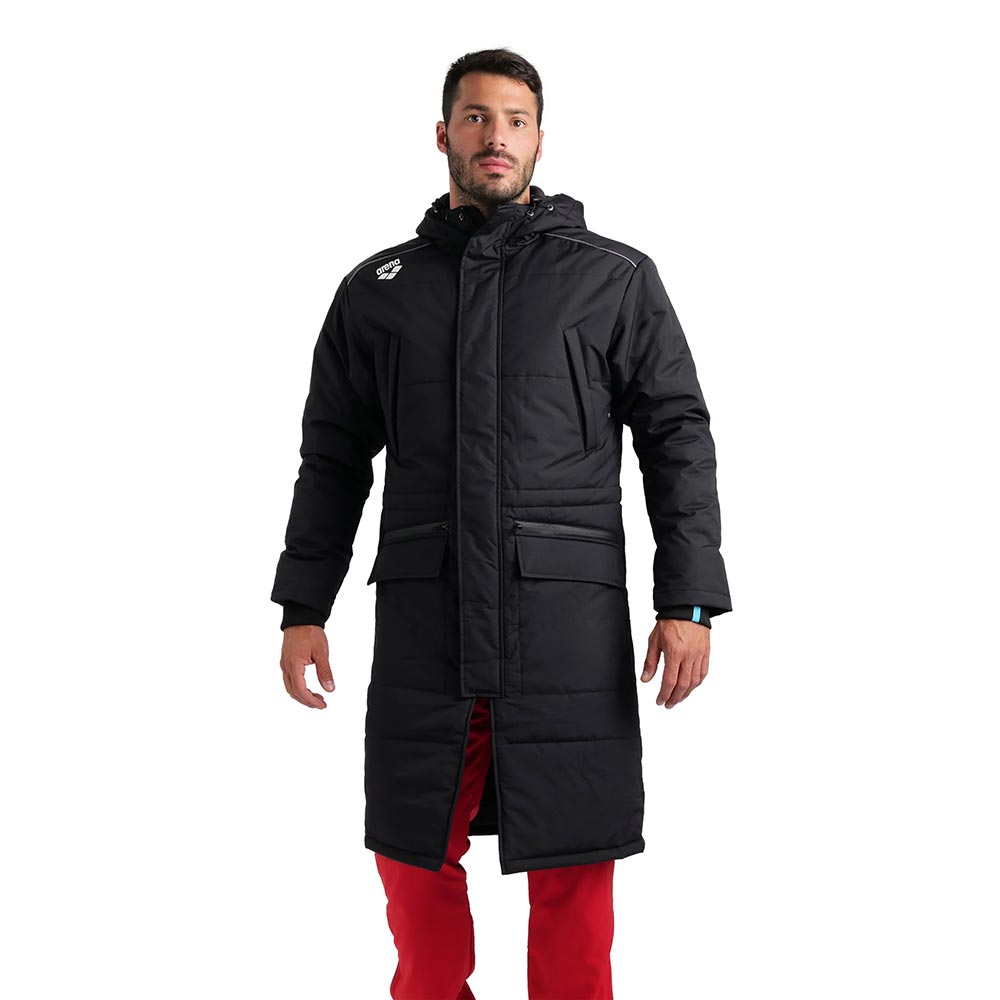 Arena unisex black long team parka jacket worn by a man in red trousers.