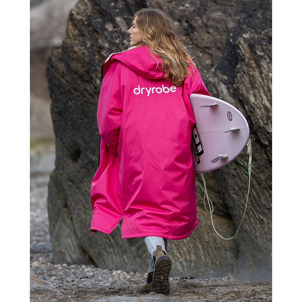 Pink Dryrobe Advance Adults Change Robe with hood, worn by a woman holding a surfboard on a beach