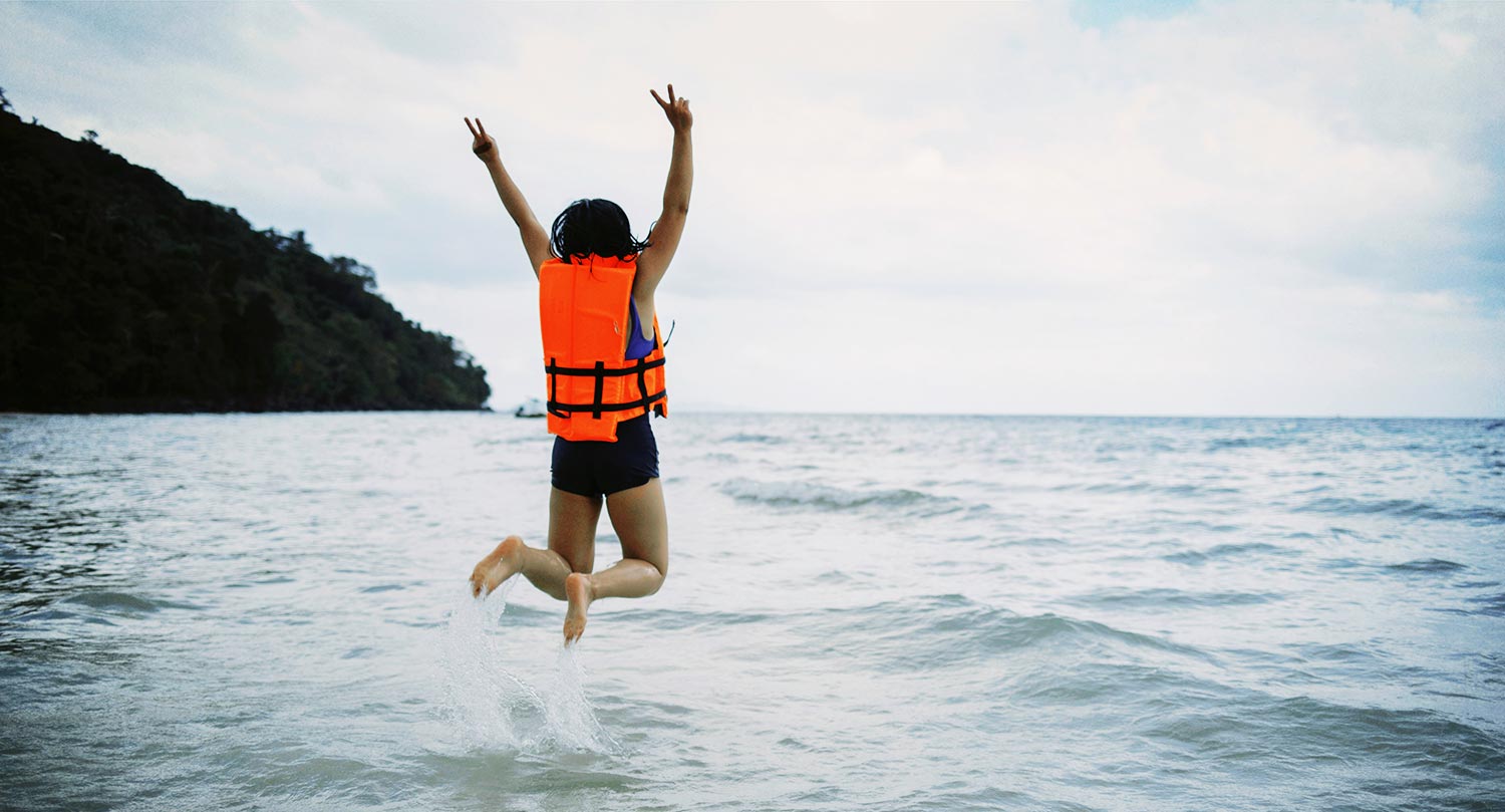A girl jumping into the ocean wearing a life jacket. This shows Swim Safe's commitment to water safety as part of their product range.